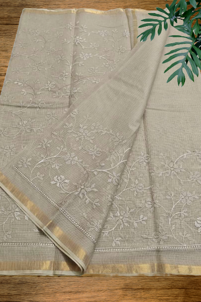 Mridula grey Kota cotton saree with floral embroidery and golden border placed on wooden surface