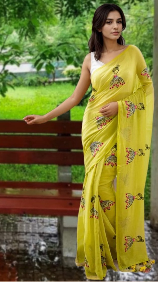 Woman wearing Mridula’s neon green mul cotton saree with colorful doll embroidery, standing near a red bench in a garden