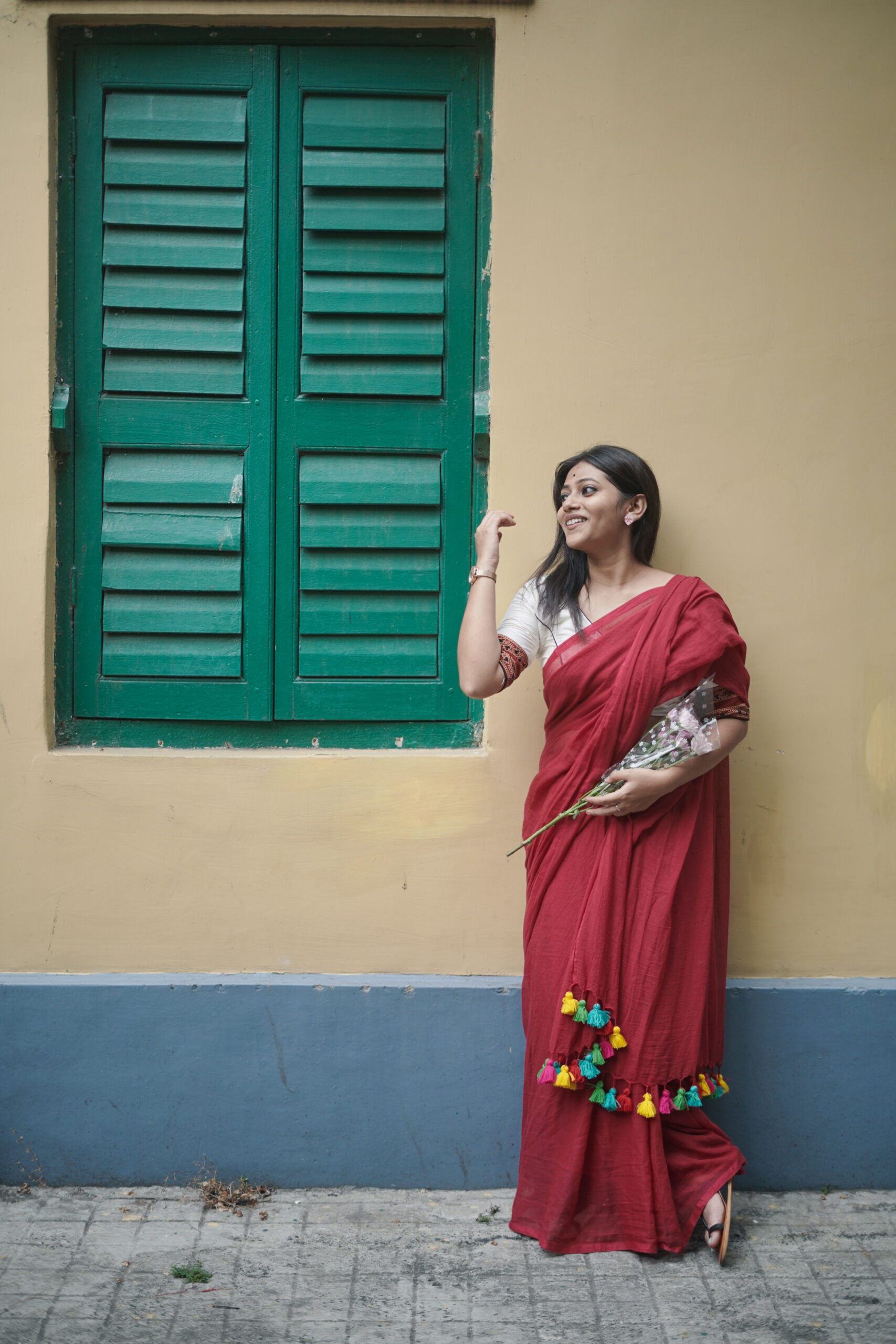 Woman in maroon Mridula mul cotton plain saree with colorful tassels holding flowers