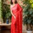 Woman wearing Mridula red mul cotton saree with white floral embroidery, standing near indoor plants